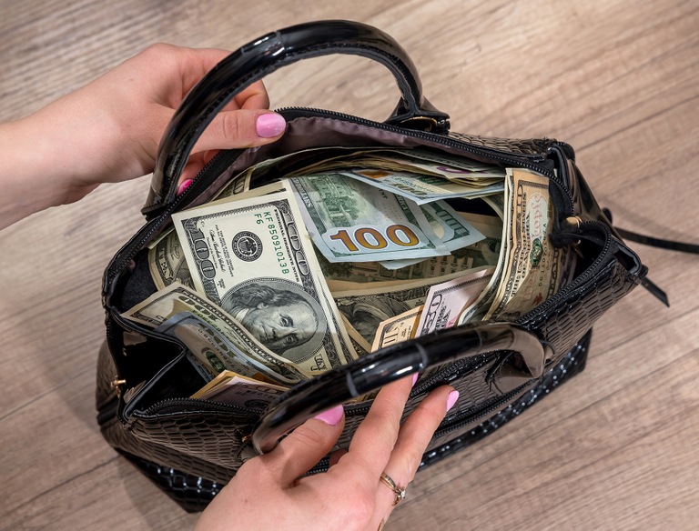 Stock image depicting woman holding open purse filled with currency.